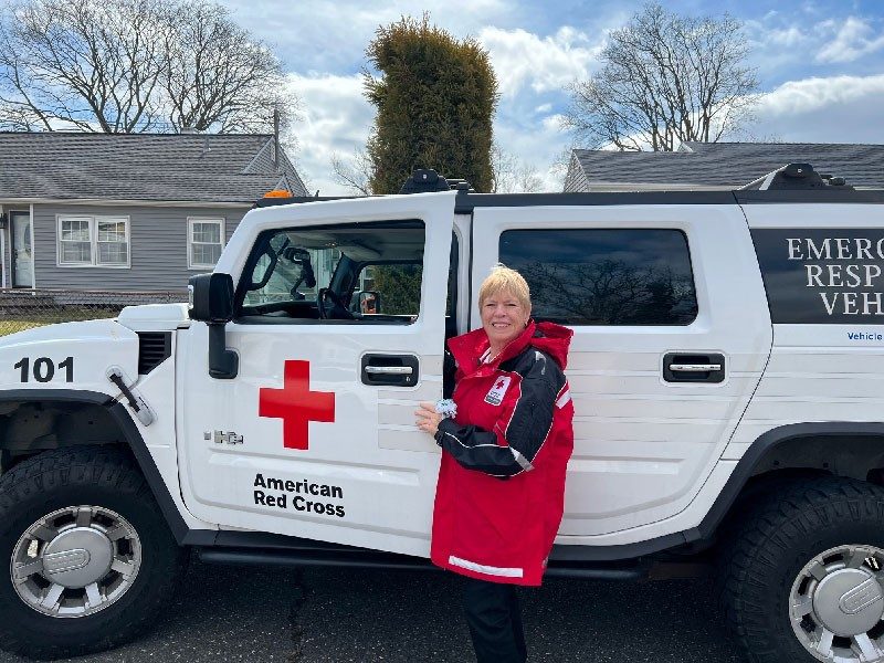 red cross volunteer standing in front of a red cross car