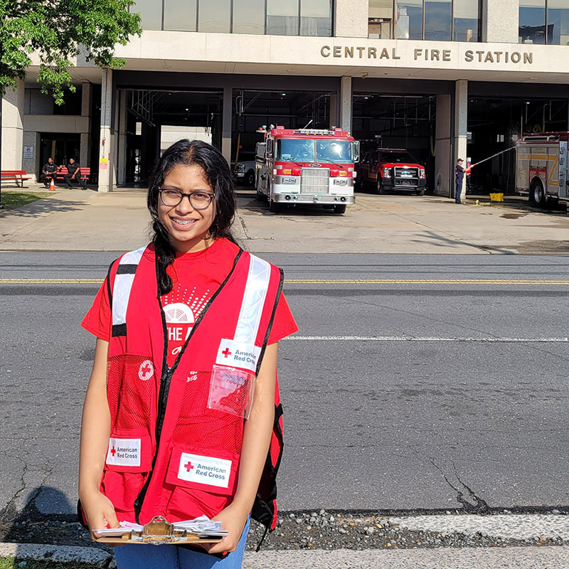 Ananya Uddanti in Red Cross vest with fire engine behind her