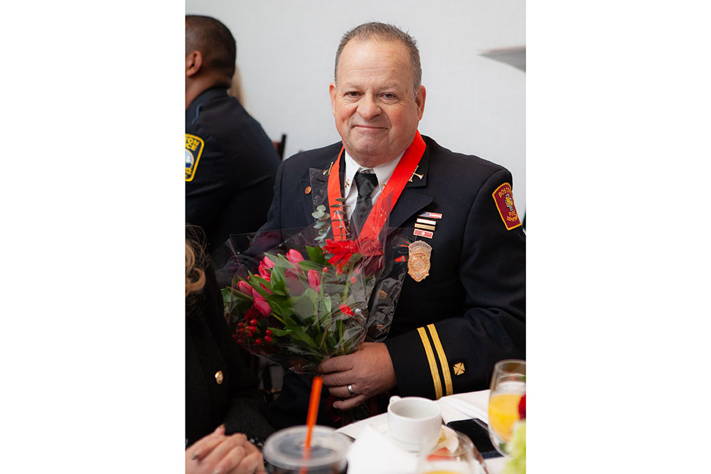 Firefighter Pat Murphy wearing medal and holding a bouquet of flowers