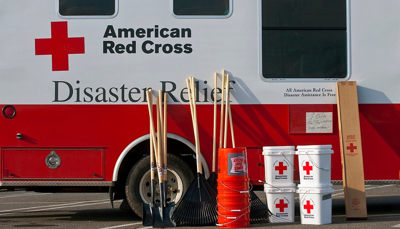 Shovels, rakes, and 5 gallon buckets next to American Red Cross Disaster Relief vehicle.