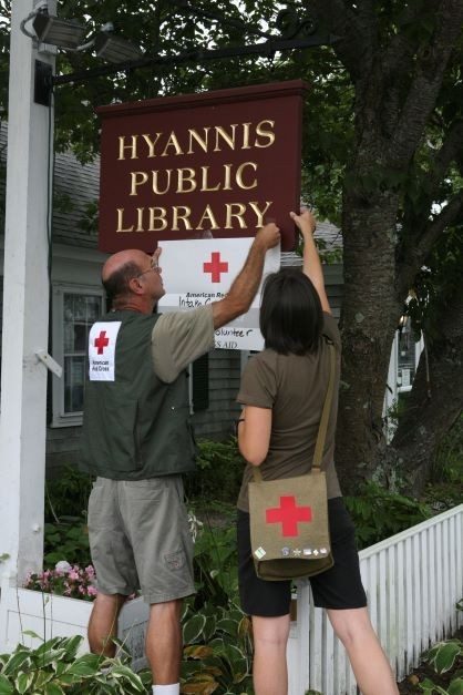 Red Cross volunteers hanging Red Cross sign outside library.