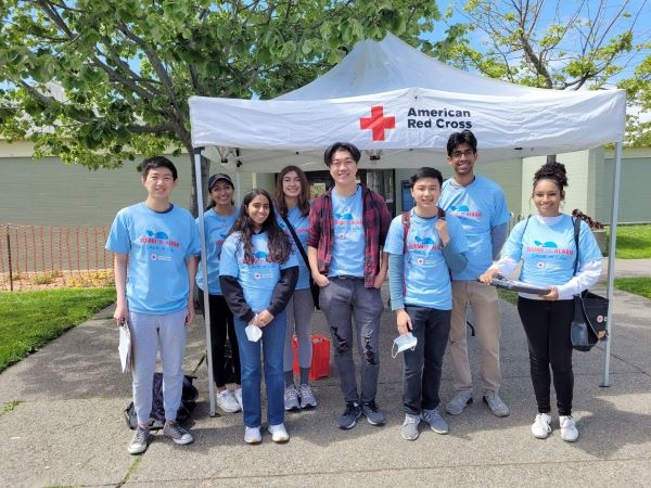 eight teens standing side by side in red cross shirts