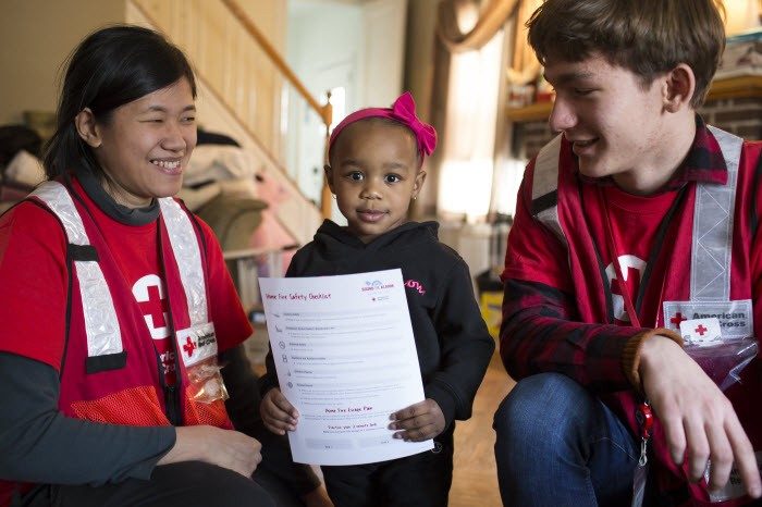 two red cross volunteers with a child holding a home fire safety plan