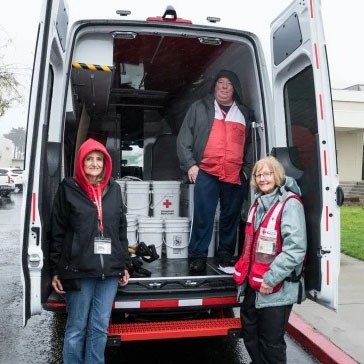 3 Red Cross volunteers in back of truck with supplies.