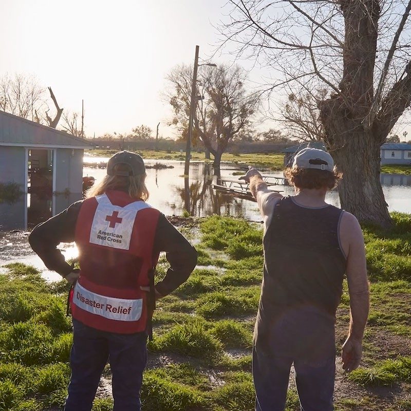 Red Cross volunteer helping man who is pointing at flooding.