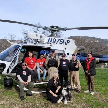 Red Cross volunteers and pilots group shot in front of helicopter.