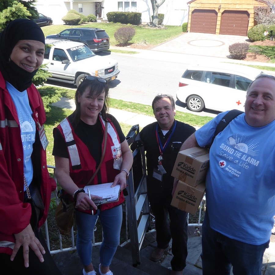 Red Cross volunteers posing on steps holding smoke alarms to install