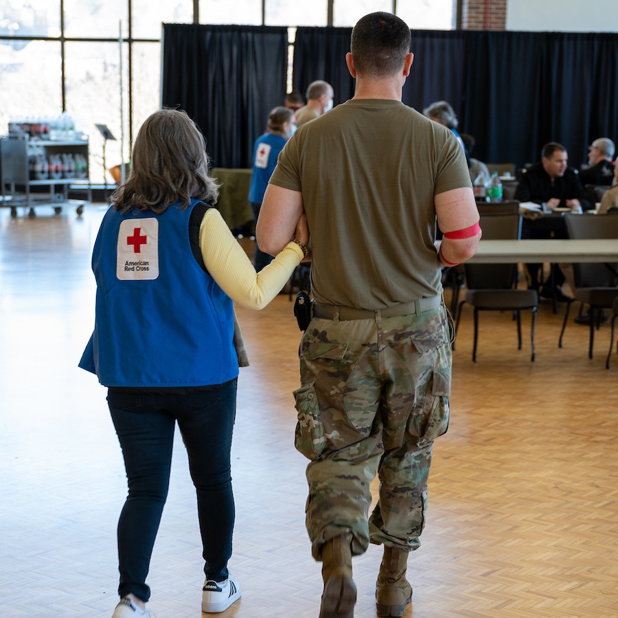 Women in Red Cross blue vest and West Point serviceman walking together to give blood