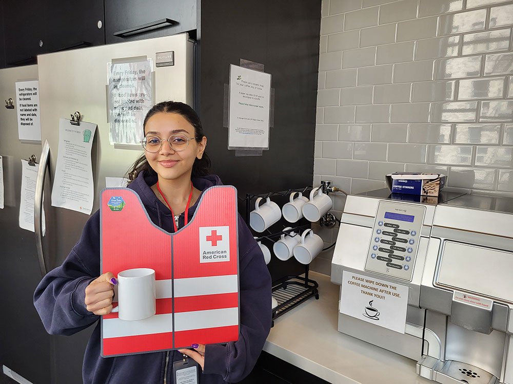 Buthaina Al Zubair holding ceramic mug with cardboard cutout of Red Cross vest