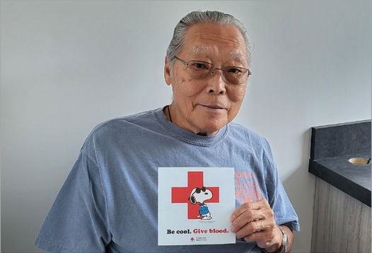 Eddie Fong holding a "Be cool. Give blood." sign.