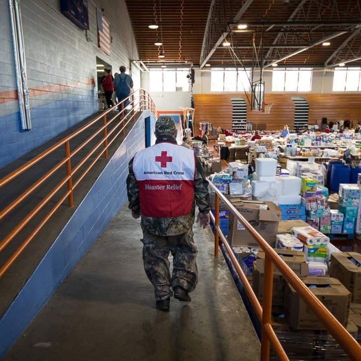 John Sternberg walking in warehouse with Red Cross vest over military clothing.