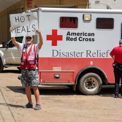 Red Cross volunteer holding hot meals sign.