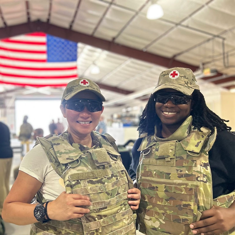 Christiana Ilufoye and Donna Gordon Green in military attire with Red Cross logo on hat and American flag in background