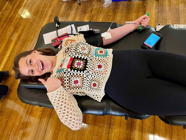 Woman laying on cot donating blood giving a thumbs up sign.