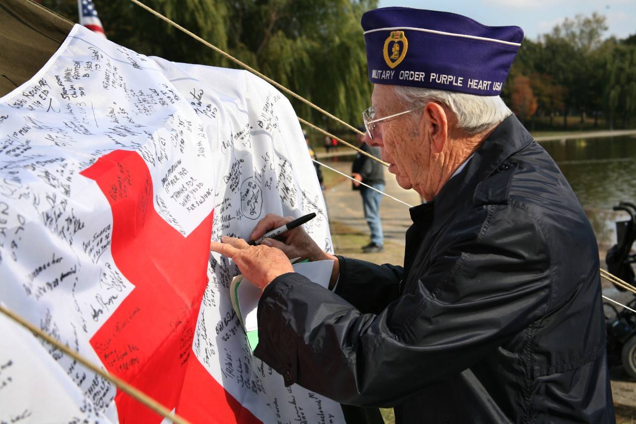 A WWII veteran signs an American Red Cross flag at the Service to the Armed Forces tent on the National Mall.