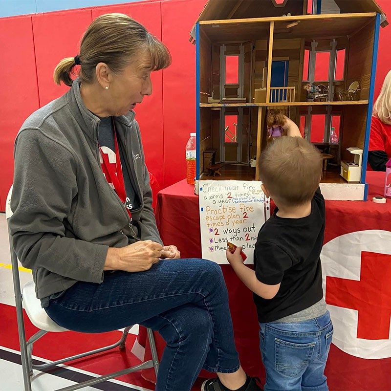 Red Cross volunteer watching child play with doll house.