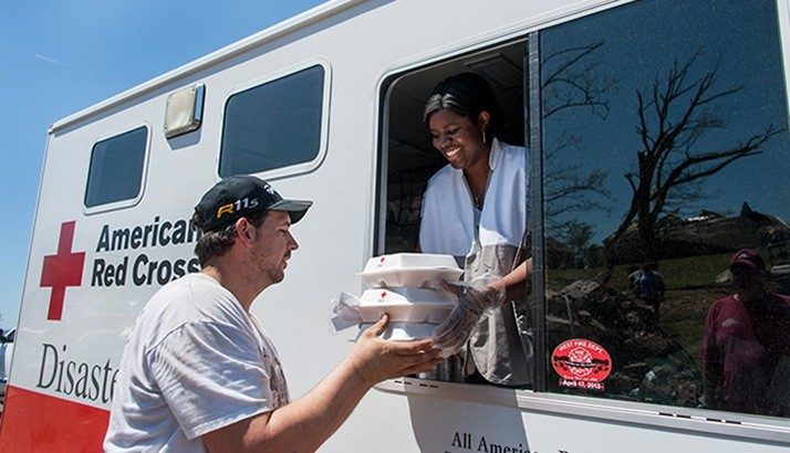 Red Cross volunteer in Red Cross van handing food to man through window