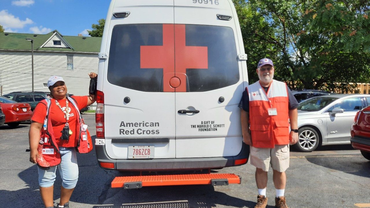 Two Red Cross volunteers standing at the back of a Red Cross van