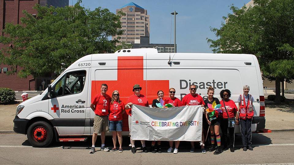 Group of Red Cross volunteers standing in front of Red Cross vehicle holding a celebrating diversity banner