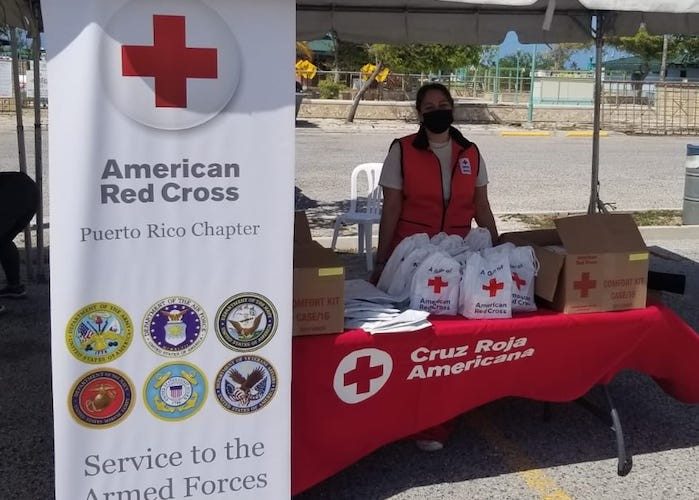 Red Cross volunteer wearing mask and vest at table with Red Cross bags and boxes