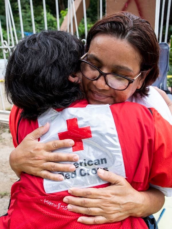 Red Cross volunteer hugging woman with glasses