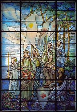 10009_003 - September 7, 2006 - Tiffany Windows at the Board of Governors Hall - Washington D.C. - Photo: Hector Emanuel - no release needed - Right Window --

Three beautiful Tiffany windows are located in the elegant Board of Governors Hall at American Red Cross national headquarters in Washington, D.C. They are reputed to be the largest surviving suite of Tiffany windows still in their original location (except for those in churches). 

The Left Tiffany Window was funded by the Women's Relief Corps of the North. It shows the legendary Saint Filomena, famed for her healing powers, surrounded by women symbolizing different virtues such as hope, mercy, faith, and charity. These virtues are an integral part of the symbolism of the national headquarters building , which was conceived as a "Memorial to the Heroic Women of the Civil War." The first woman pictured in the window carries a shield emblazoned with the Red Cross emblem. Also included in the scene are a mother holding her child and a maiden carrying the Red Cross banner. 

The Central Tiffany Window, a joint gift from the Women's Relief Corps of the North and the United Daughters of the Confederacy, symbolizes the healing of a formerly divided nation. It portrays an army of gallant knights in armor, mounted on horses and carrying spears. The central figure, astride a white horse bedecked with jeweled trappings, carries a large flag with the Red Cross emblem. An injured warrior lies at the horse's feet and receives food and aid from a compassionate comrade. This scene underscores the Red Cross commitment to provide assistance on the battlefield. 

The Right Tiffany Window, funded by the United Daughters of the Confederacy, features Una from Edmund Spenser's "Faerie Queene," who represents truth and fortitude. Una's apron is filled with roses--symbols of good deeds. She is accompanied by a maiden holding a cross and another young woman who carries the lamp of wisdom. Behind her are maidens with banners symbolizi