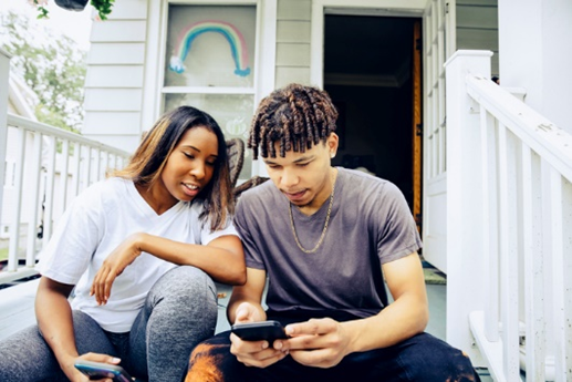 Two young adults sitting on a porch using their phones