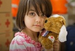 Young girl holding a teddy bear.  Teddy bear has a Red Cross bandage on its arm.