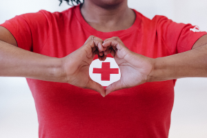 Woman making a heart shape with her hands around Red Cross logo