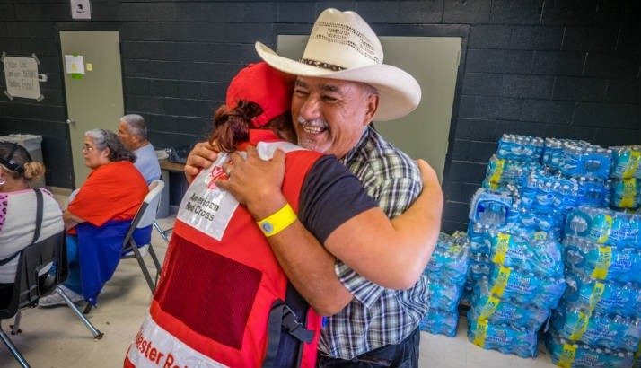 Red Cross volunteer giving a hug to man wearing a cowboy hat
