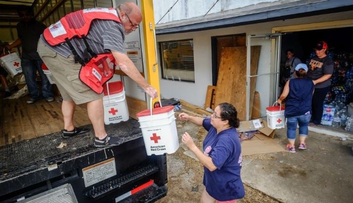 Man in Red Cross vest standing in a box truck and handing a Red Cross bucket to another volunteer