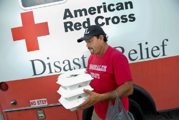 Man standing in front of a Red Cross food truck holding three meals in styrofoam take-out boxes