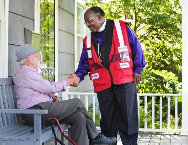Red Cross volunteer shaking hands with man sitting on bench.