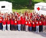 Color photograph of a large group of Red Cross volunteers in Red Cross t-shirts in front of Red Cross disaster vehicles
