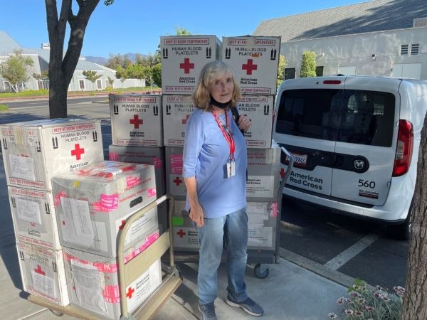 Barbara Atlas standing next to Red Cross boxes on carts