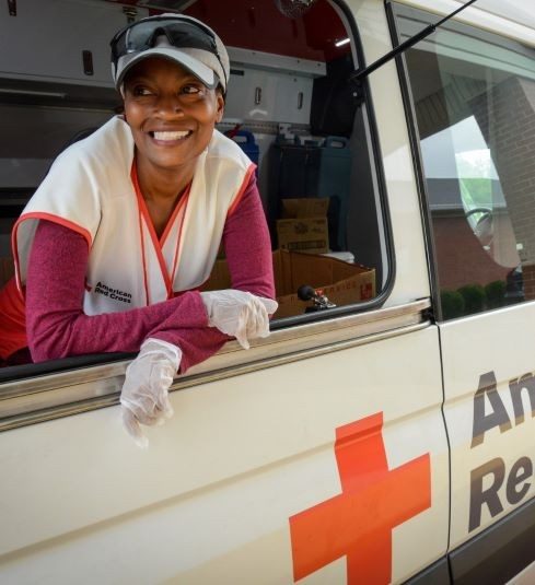 Red Cross volunteer wearing hat, glasses and rubber gloves looking out window in Red Cross vehicle