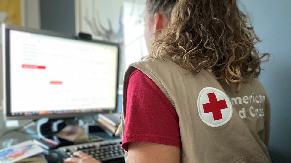 red cross volunteer sitting in front of a computer