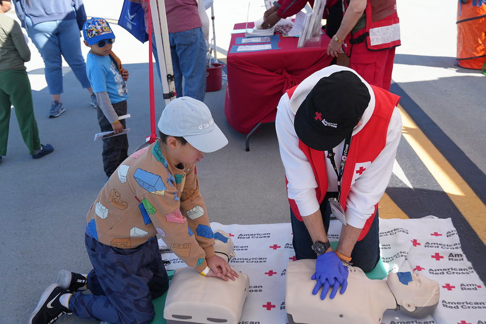 Red Cross volunteer teaching young boy CPR on manikin