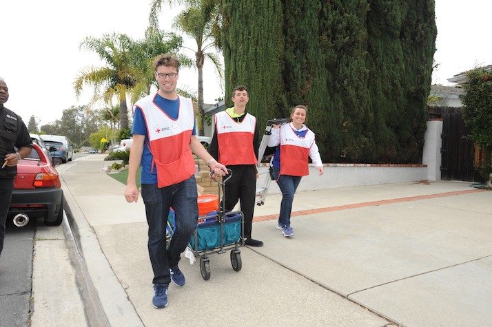 three red cross volunteers carrying cart with smoke alarm and supplies