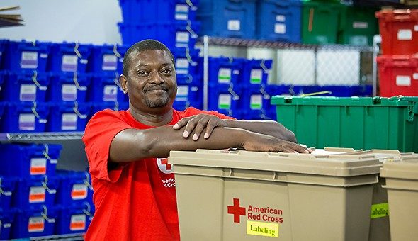 Red Cross volunteer with hands on box with boxes in background