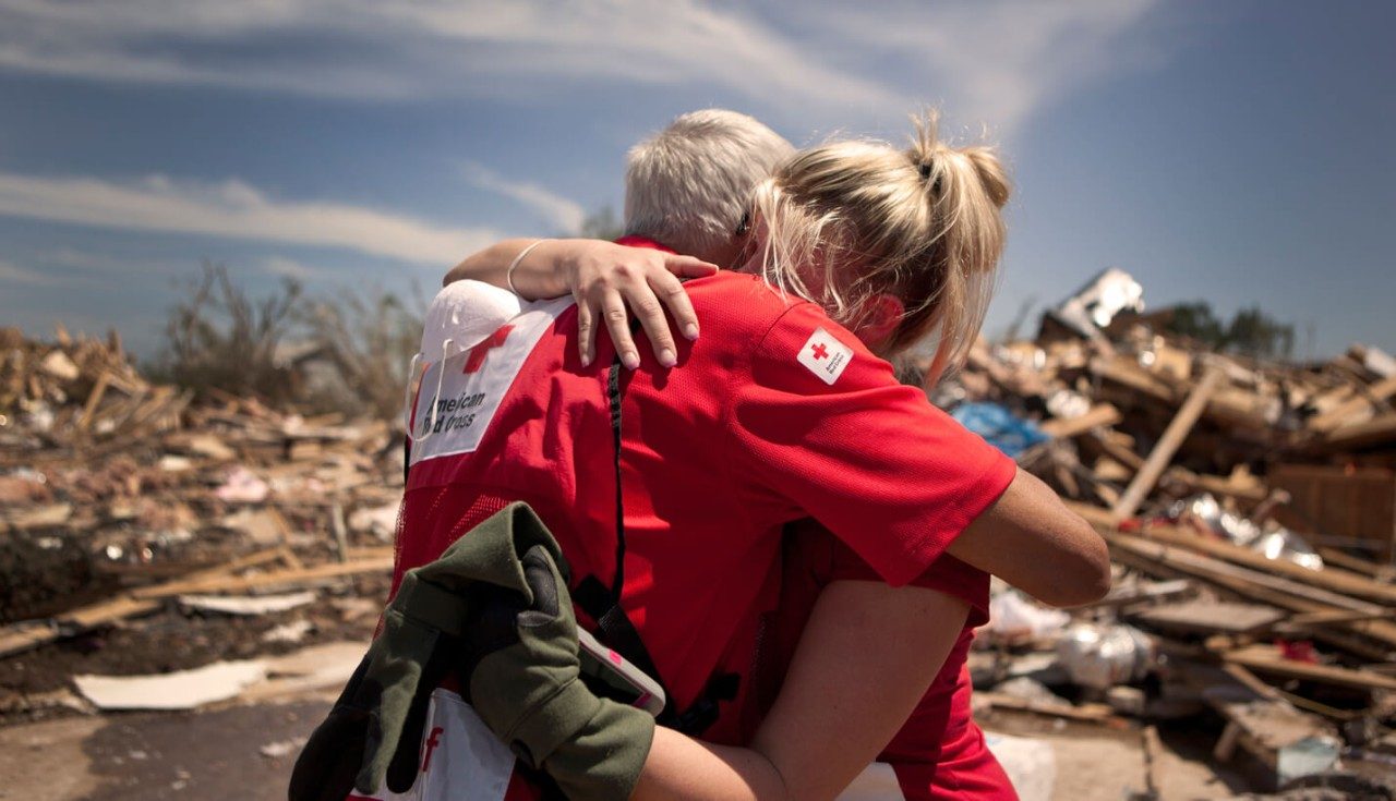 A Red Cross volunteer giving a woman a hug outside of her neighborhood damaged by a tornado.