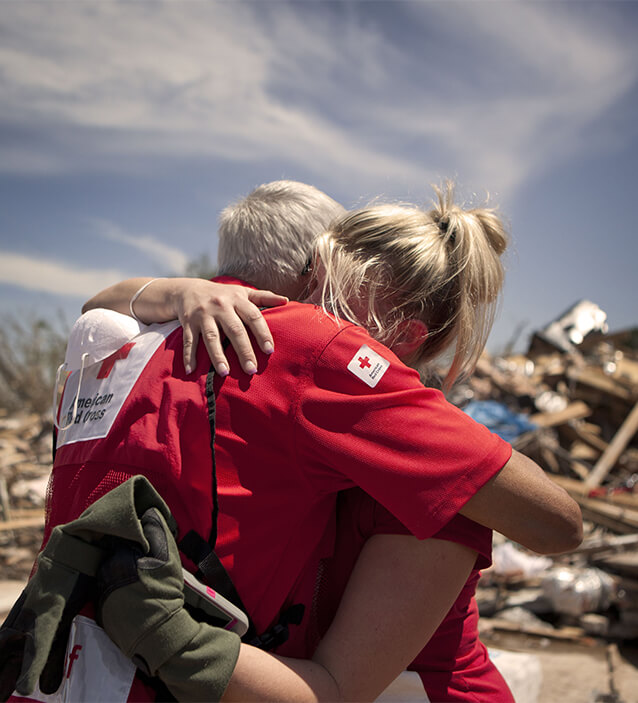 A Red Cross volunteer hugging a woman at a disaster site
