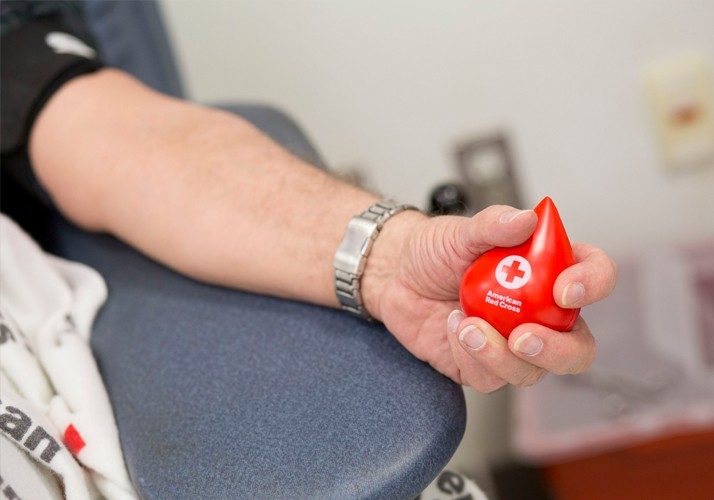 Person's hand holding Red Cross stress ball while giving blood