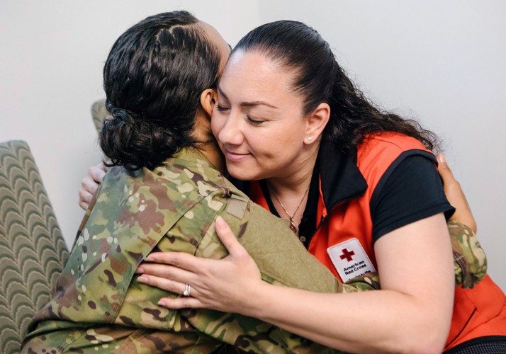 Red Cross volunteer hugging woman in military uniform
