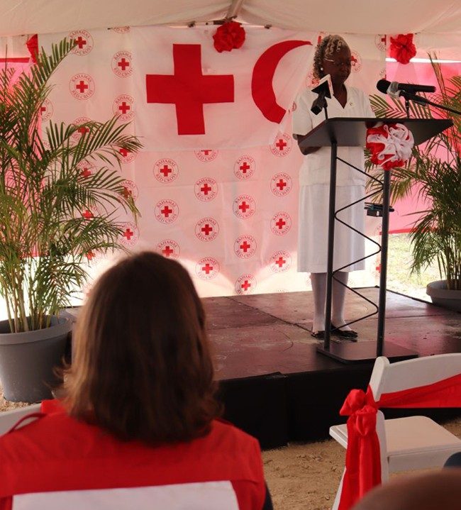 A woman is on a stage standing at a podium and speaking to Red Cross and Red Crescent members