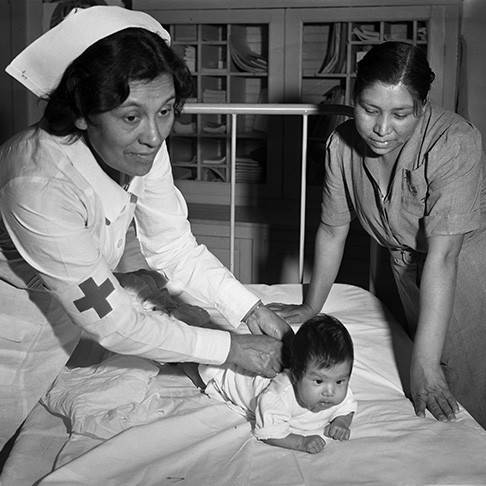 Historical Red Cross Photo - Cherokee Indian Reservation, Cherokee, North Carolina -- Mrs. Lula Owl Gloyne, Red Cross Nurse in the First World War, is back on the job again after retiring a number of years ago, teaching Mrs. Katie Ross Davis the proper care of babies. Mrs. Davis is a graduate of Haskell.