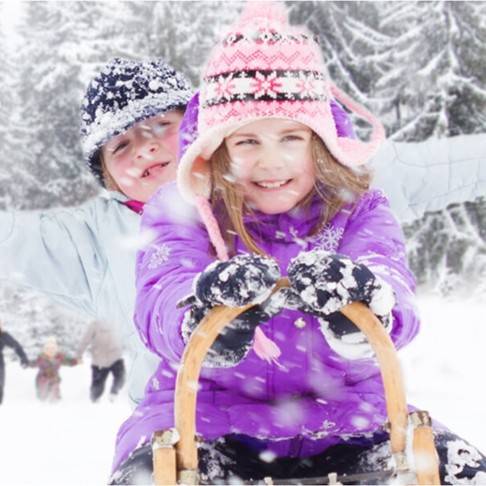 Two young kids sledding in the snow