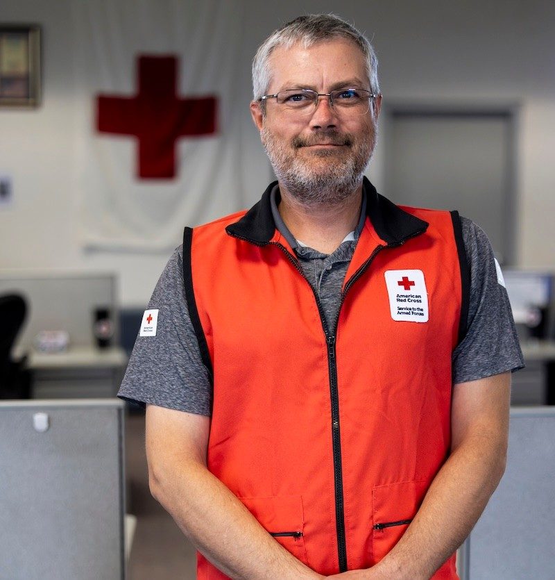 Portrait of a Caucasian man with gray hair and bread spotting a red Red Cross Hero Care vest and smiling to the camera