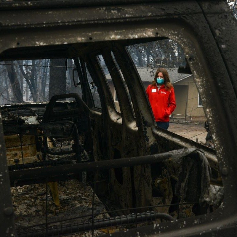 red cross volunteer looking at a burned out vehicle
