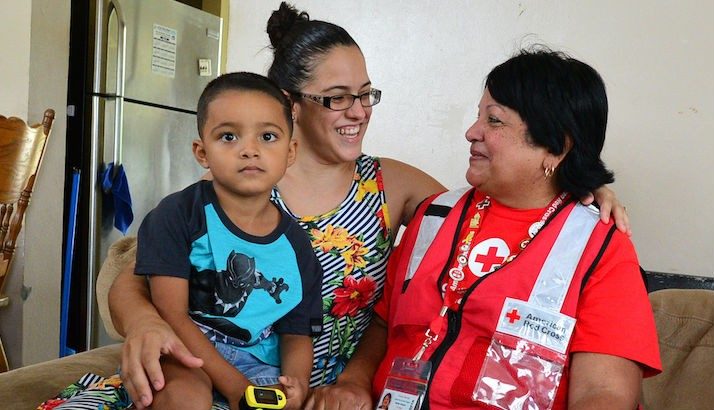 A Red Cross volunteer hugging a Hurricane Maria survivor and her child.